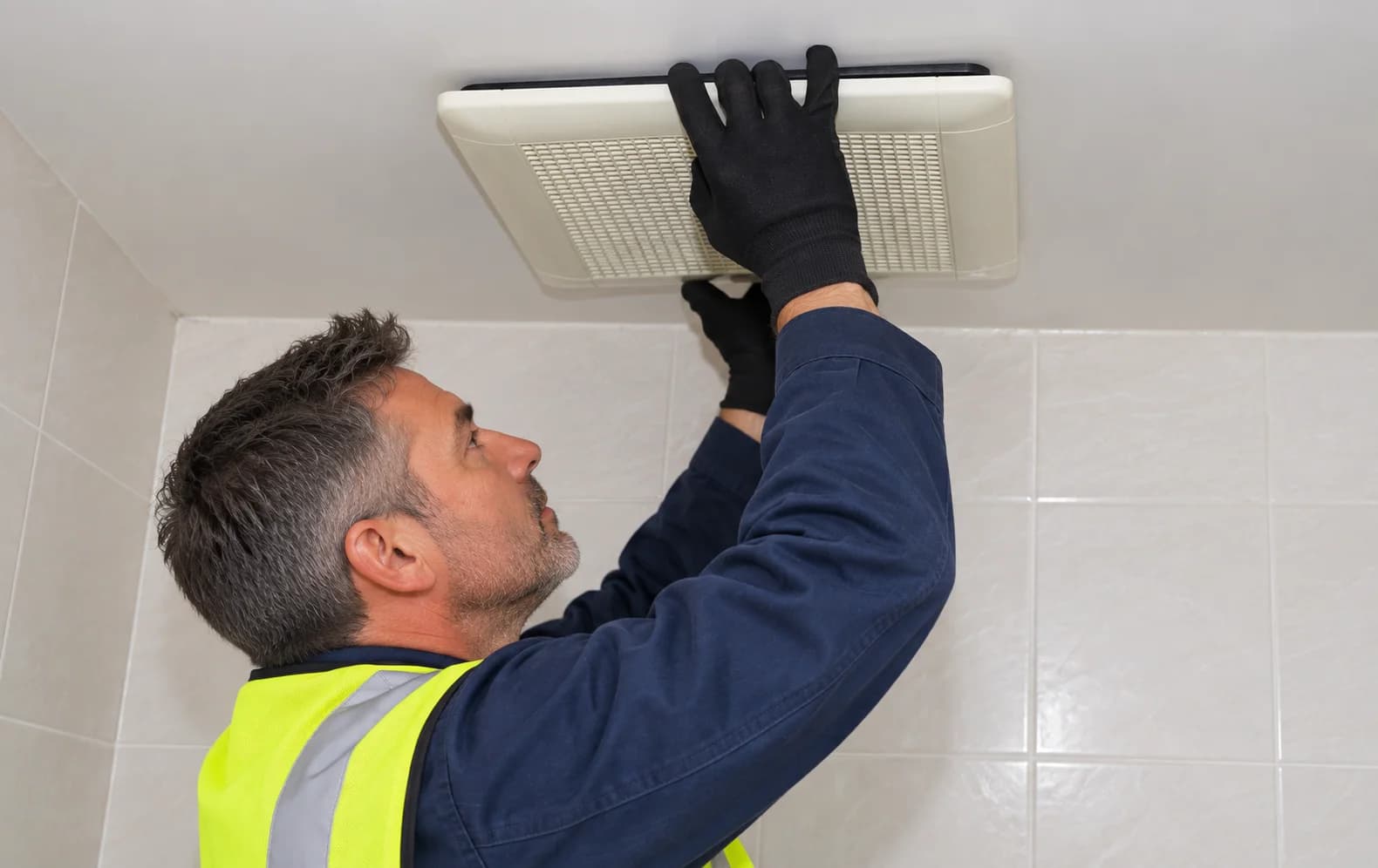 Illustration of a technician attending to a ceiling extractor fan in a bathroom.
